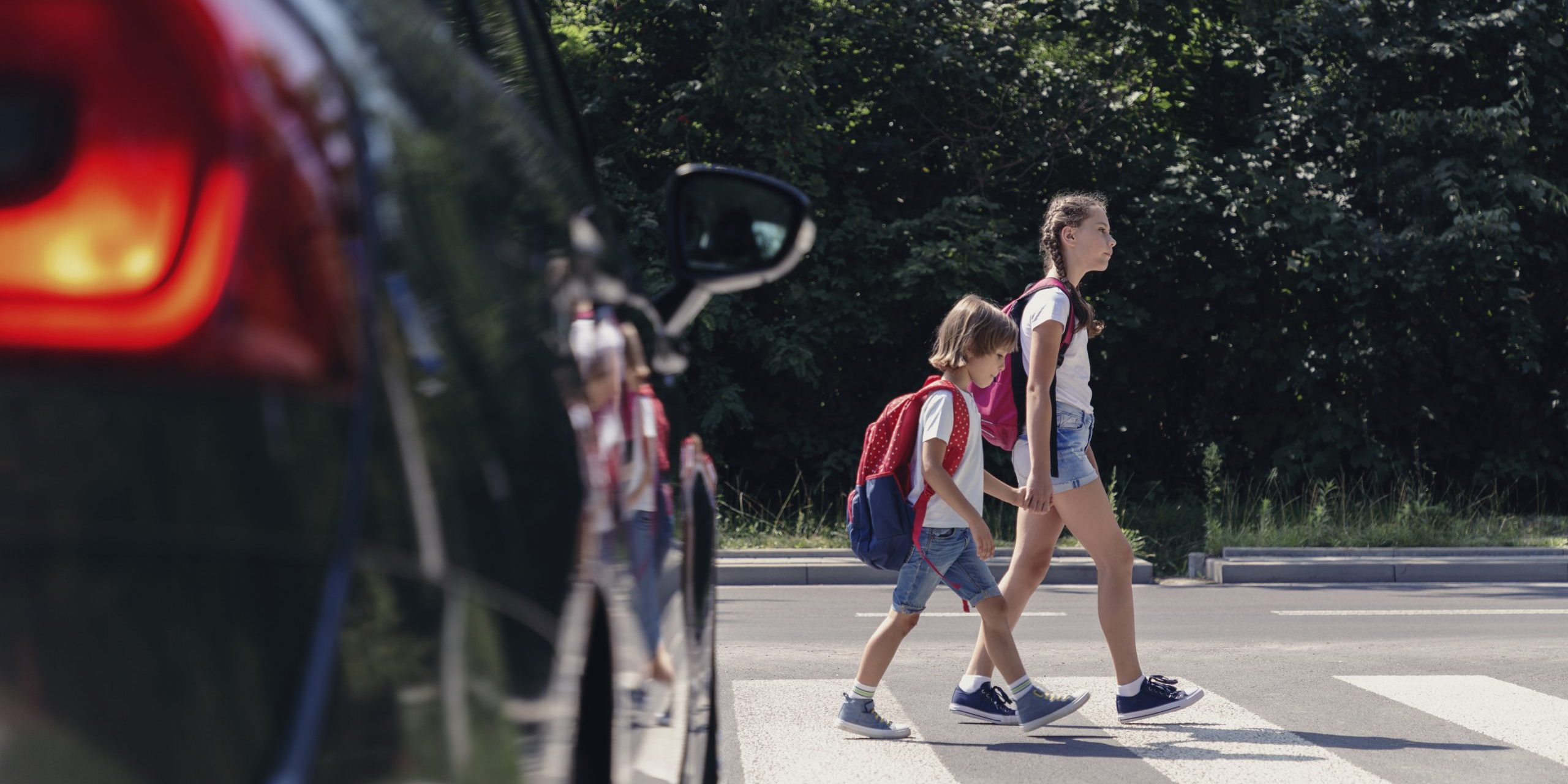 Children next to a car walking through pedestrian crossing to the school