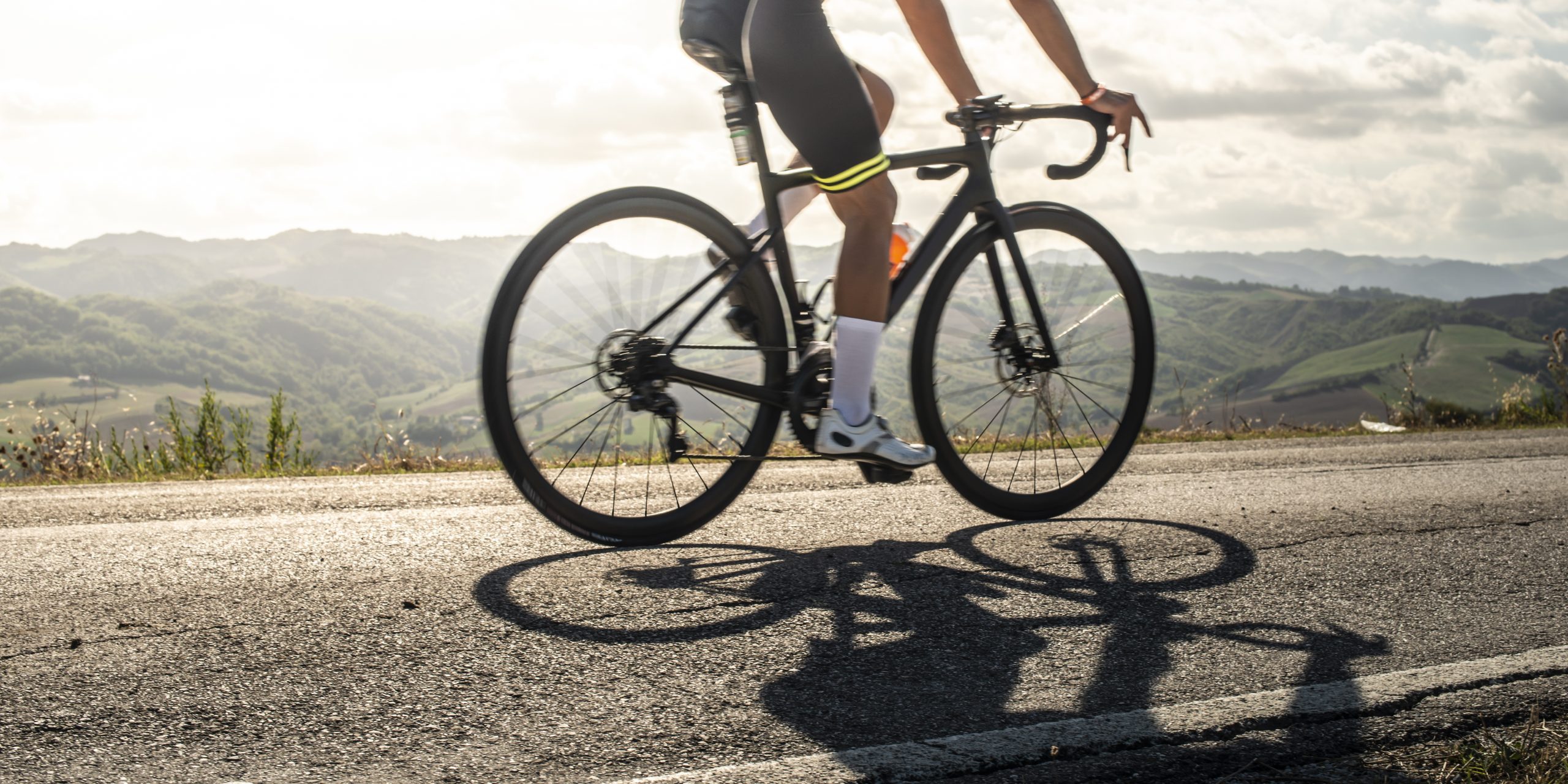 Cyclist sports on road. Sun Rays and shadows from the bike on the road. Outdoor cycling.