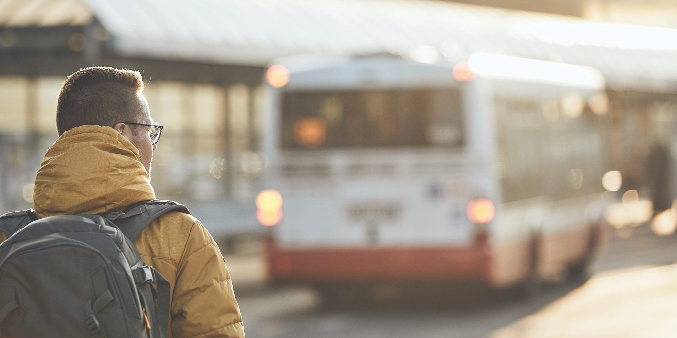 Young man with backpack walking to bus stop. City street at golden sunset. Prague, Czech Republic