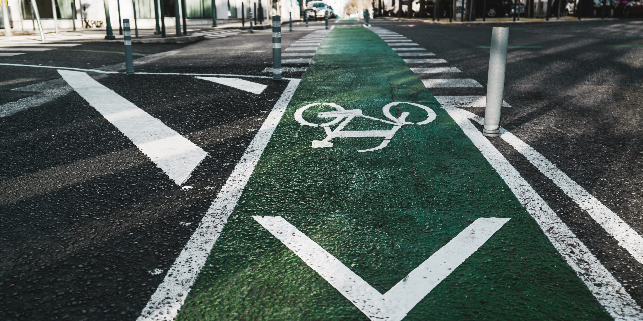 Urban wide-angle view of a modern city road in Lisbon with bicycle marking on green asphalt and two lanes of opposite directions, a pedestrian crossing in the distance, plastic posts in the foreground