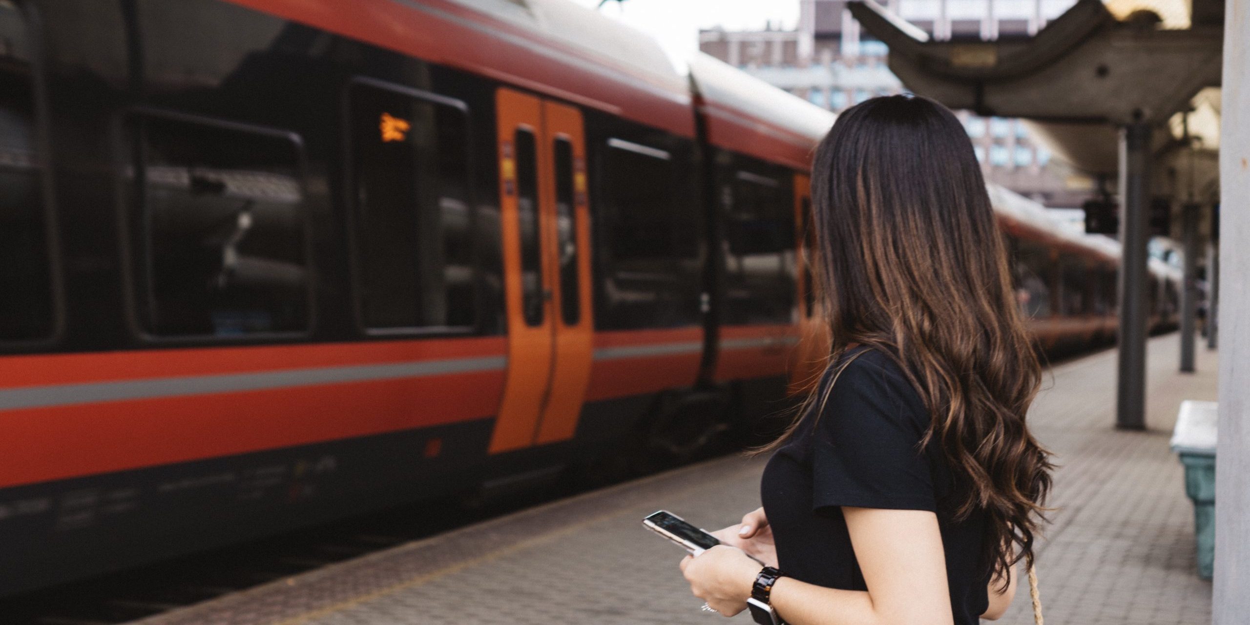 woman-using-mobile-at-train-station-waiting-for-tr-UNG7V6L